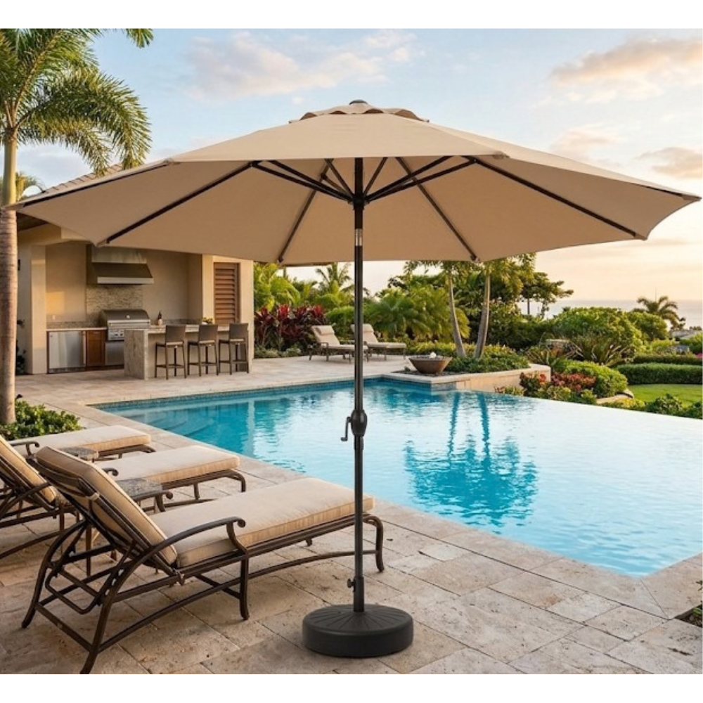 A large beige patio umbrella with a black base stands beside a swimming pool on a stone patio, with lounge chairs and tropical landscaping in the background.